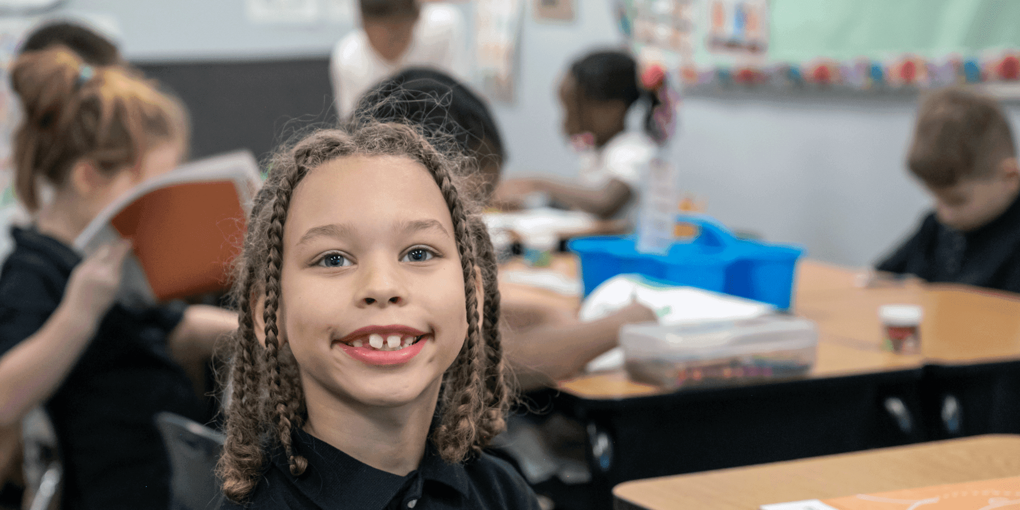 Smiling student with braided hair at a classroom desk.