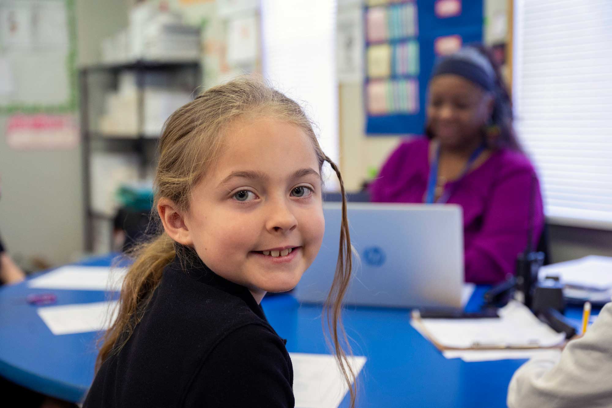Smiling student sitting at a blue classroom table.