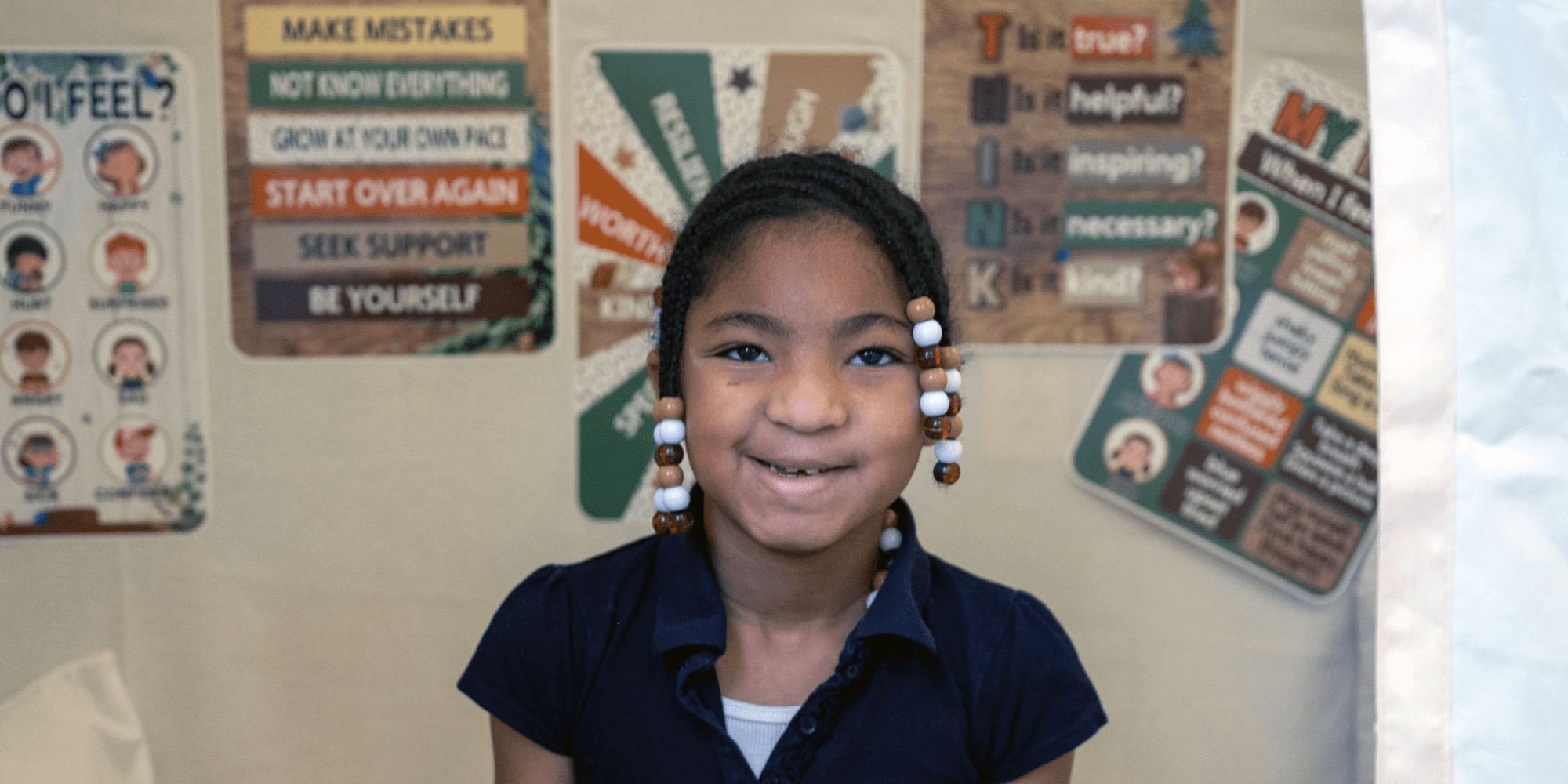 Smiling student in front of classroom posters about growth and kindness.