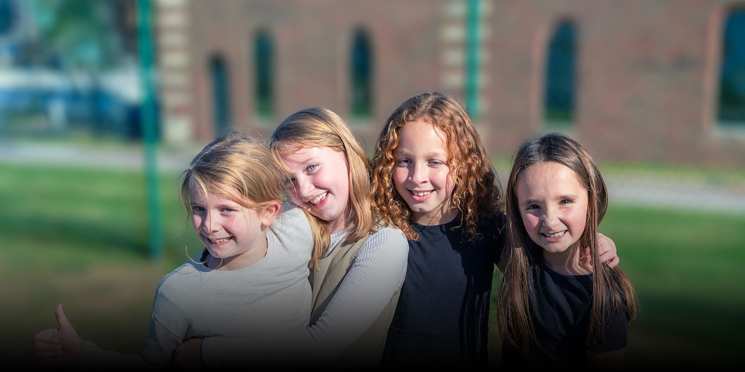 A group of smiling students standing outside embracing one another